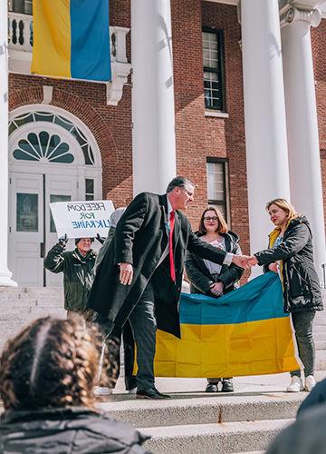 BSU 总统 Fred Clark shaking hands with students holding the Ukrainian flag in front of Boyden Hall; a man holds a sign that says Freedom for Ukraine
